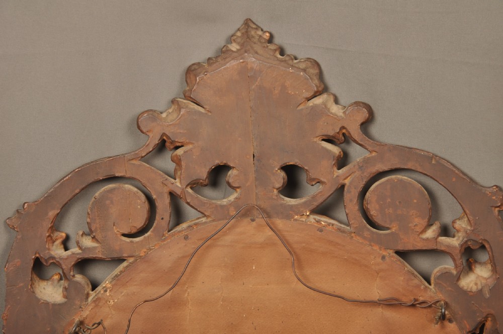 An antique oval giltwood wall mirror featuring an intricately carved openwork frame decorated with scrolling acanthus leaves, C-scrolls, rope moulding, and shell cresting. View IX