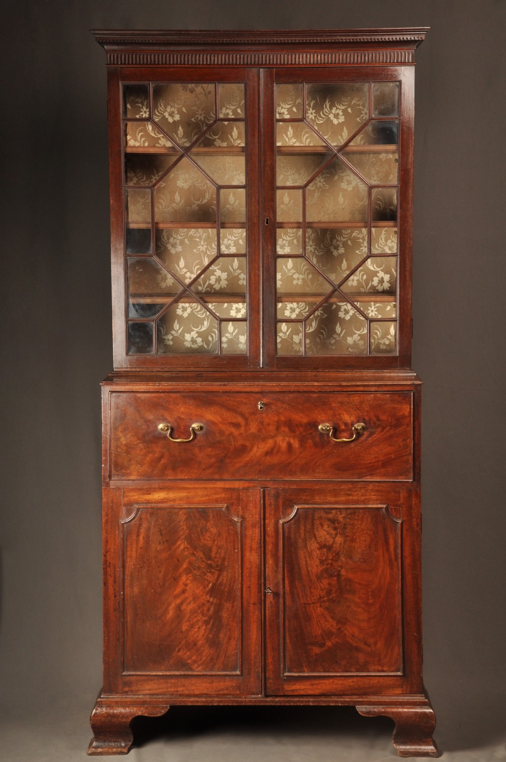 An 18th-century mahogany secretaire bookcase featuring a dentil cornice, astragal-glazed upper cabinet doors, a drop-front writing drawer with brass handles, and a two-door lower cupboard resting on bracket feet.