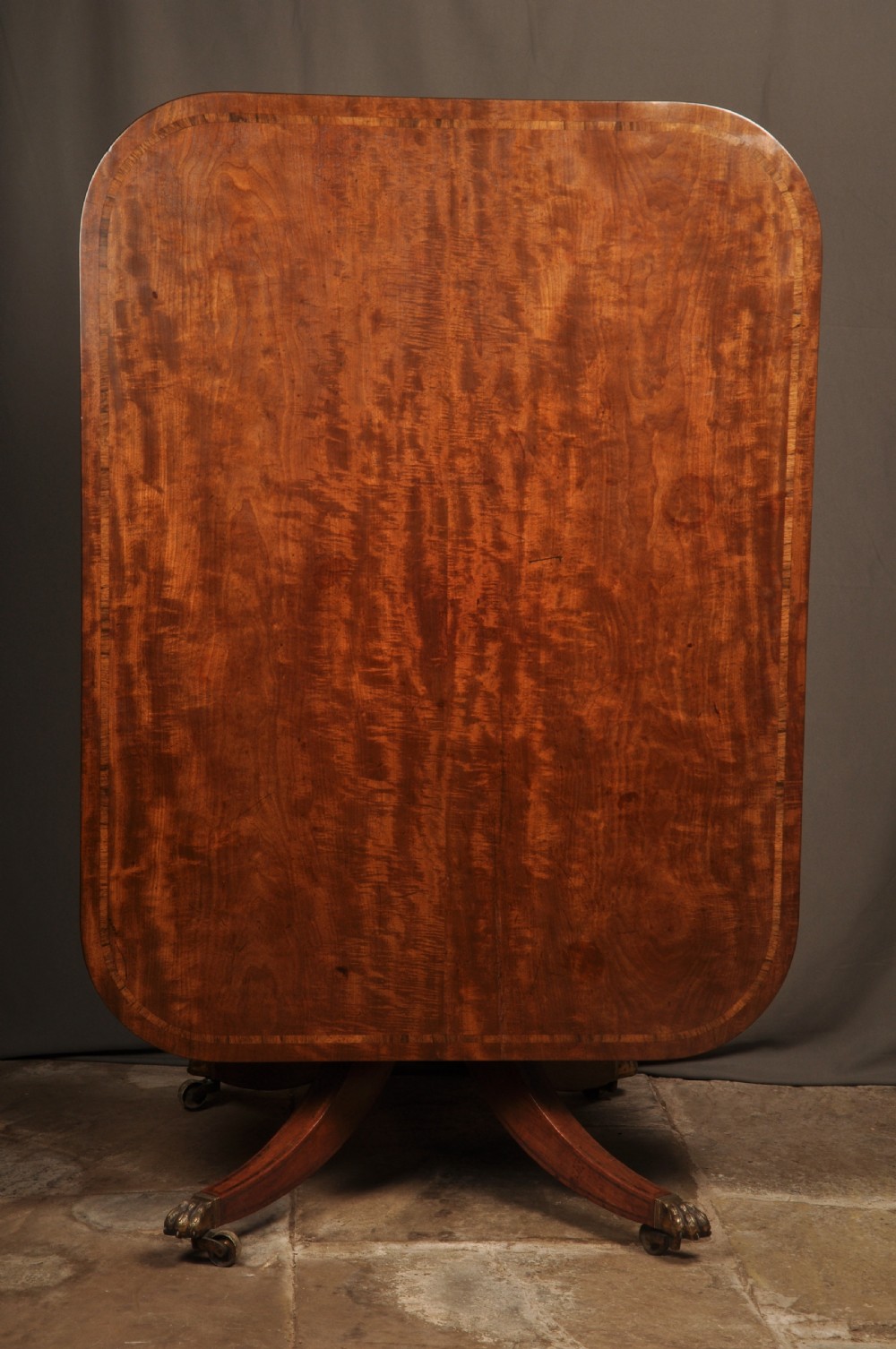 A Regency mahogany breakfast table featuring a rounded rectangular top, a turned central pedestal with acanthus carving, and four splayed legs with brass paw feet. View II