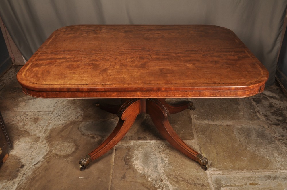 A Regency mahogany breakfast table featuring a rounded rectangular top, a turned central pedestal with acanthus carving, and four splayed legs with brass paw feet. View III