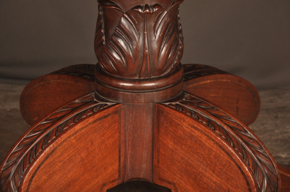 A Regency mahogany breakfast table featuring a rounded rectangular top, a turned central pedestal with acanthus carving, and four splayed legs with brass paw feet. View V