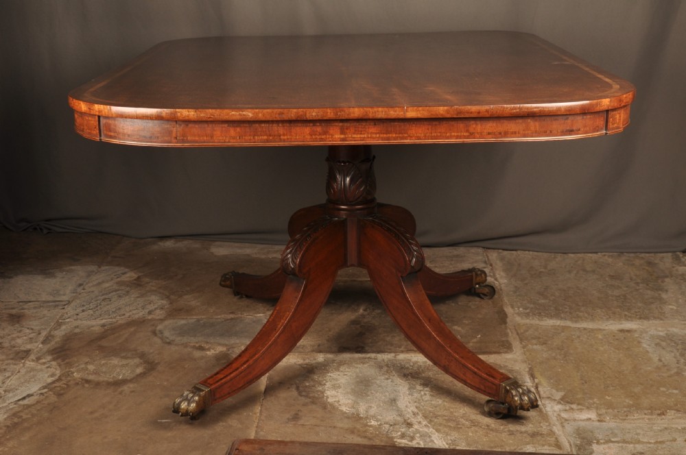 A Regency mahogany breakfast table featuring a rounded rectangular top, a turned central pedestal with acanthus carving, and four splayed legs with brass paw feet. View VII