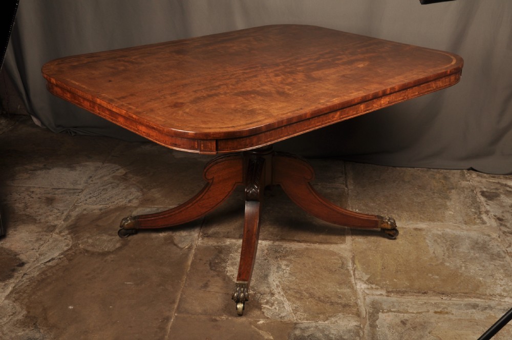 A Regency mahogany breakfast table featuring a rounded rectangular top, a turned central pedestal with acanthus carving, and four splayed legs with brass paw feet. View VIII