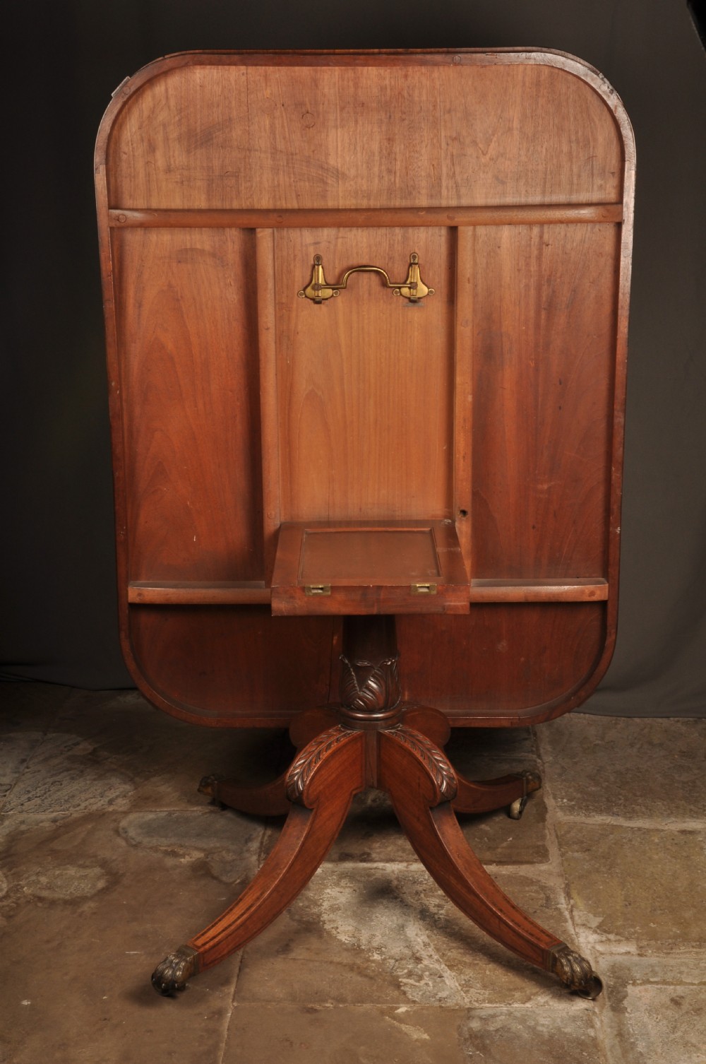 A Regency mahogany breakfast table featuring a rounded rectangular top, a turned central pedestal with acanthus carving, and four splayed legs with brass paw feet. View X