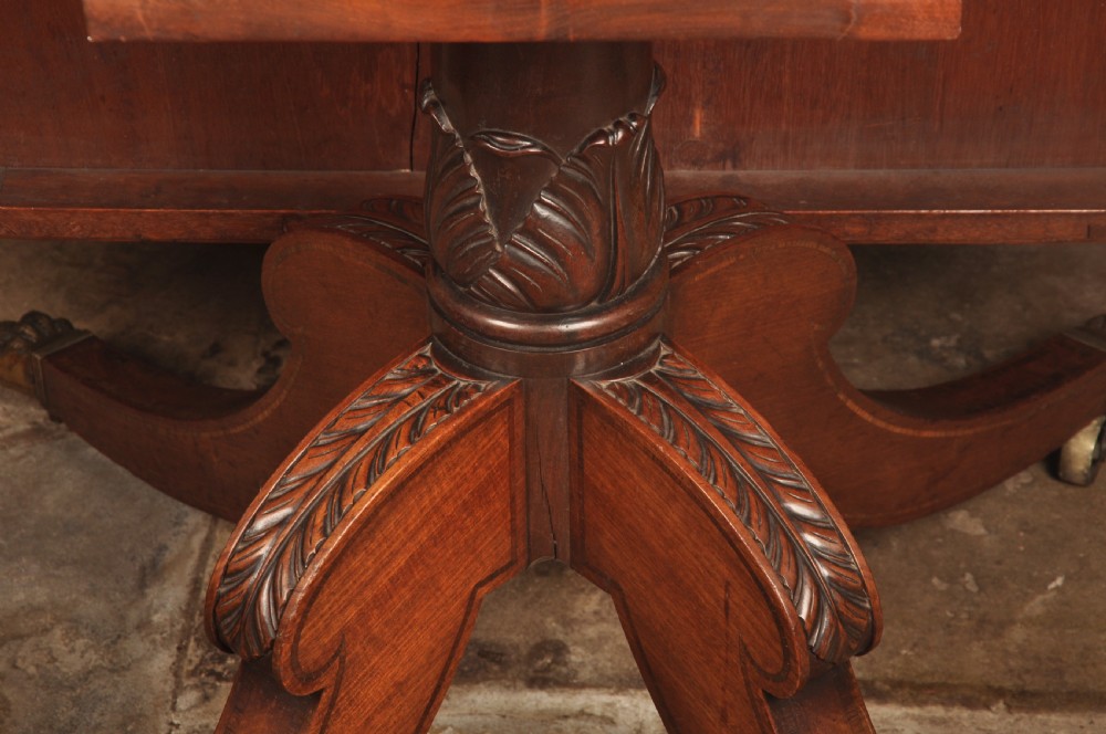 A Regency mahogany breakfast table featuring a rounded rectangular top, a turned central pedestal with acanthus carving, and four splayed legs with brass paw feet. View XI