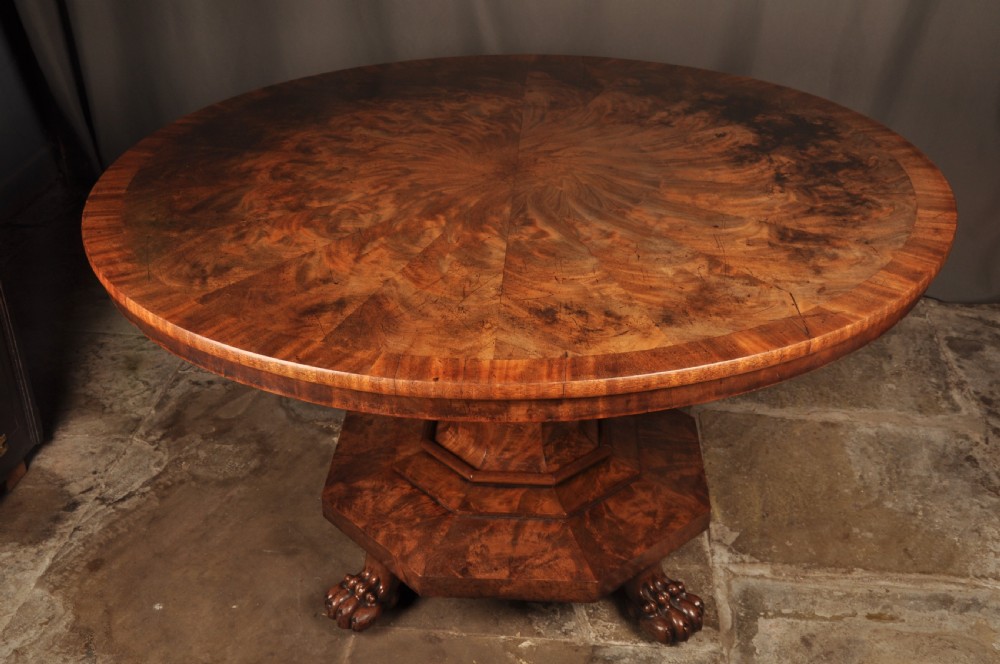 A circular Regency mahogany breakfast table featuring flame mahogany radial veneers, a faceted pedestal, and carved lion paw feet.