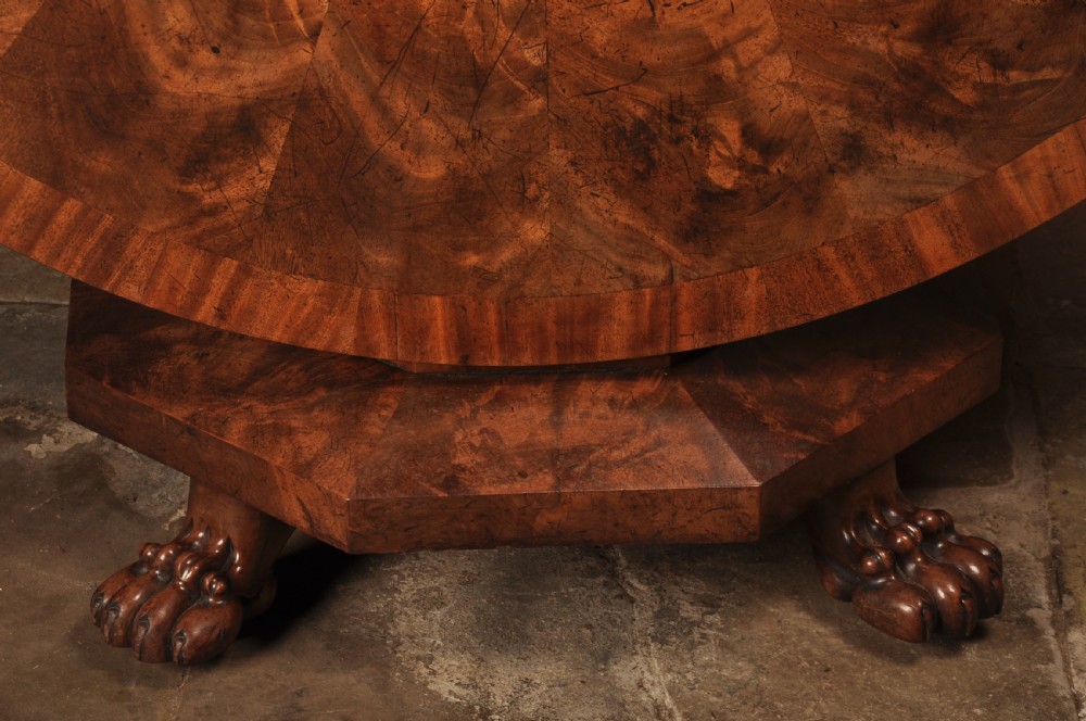 A circular Regency mahogany breakfast table featuring flame mahogany radial veneers, a faceted pedestal, and carved lion paw feet. View II