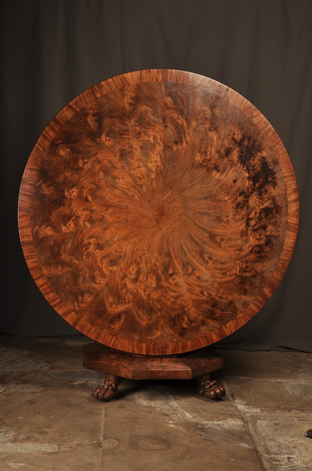 A circular Regency mahogany breakfast table featuring flame mahogany radial veneers, a faceted pedestal, and carved lion paw feet. View VI