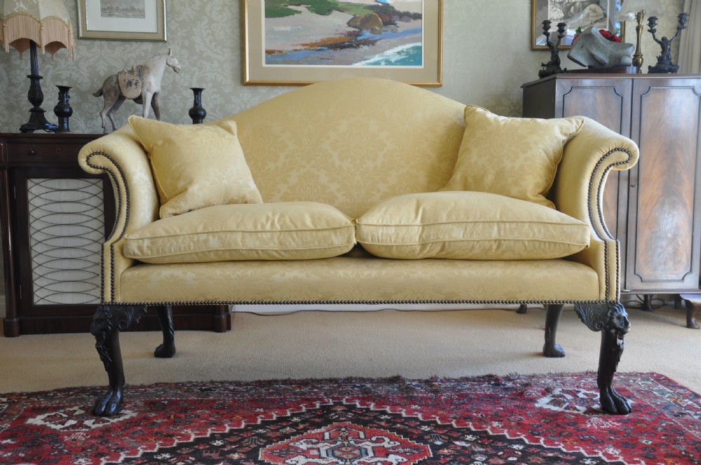 A 19th-century camelback settee upholstered in patterned yellow damask fabric with brass studding and carved mahogany legs featuring lion mask motifs.