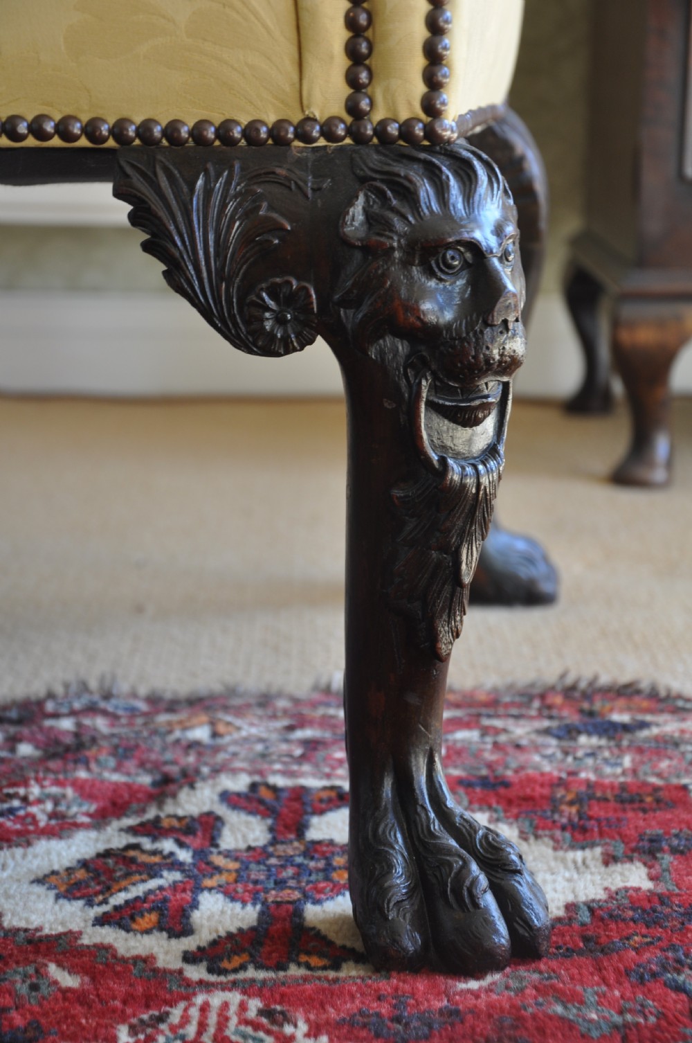 A 19th-century camelback settee upholstered in patterned yellow damask fabric with brass studding and carved mahogany legs featuring lion mask motifs. View III
