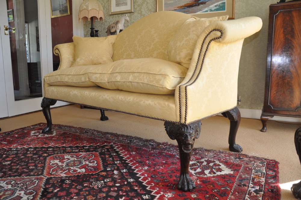 A 19th-century camelback settee upholstered in patterned yellow damask fabric with brass studding and carved mahogany legs featuring lion mask motifs. View IV