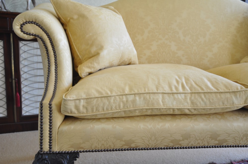 A 19th-century camelback settee upholstered in patterned yellow damask fabric with brass studding and carved mahogany legs featuring lion mask motifs. View V