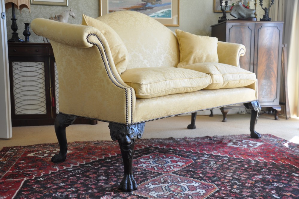 A 19th-century camelback settee upholstered in patterned yellow damask fabric with brass studding and carved mahogany legs featuring lion mask motifs. View VIII