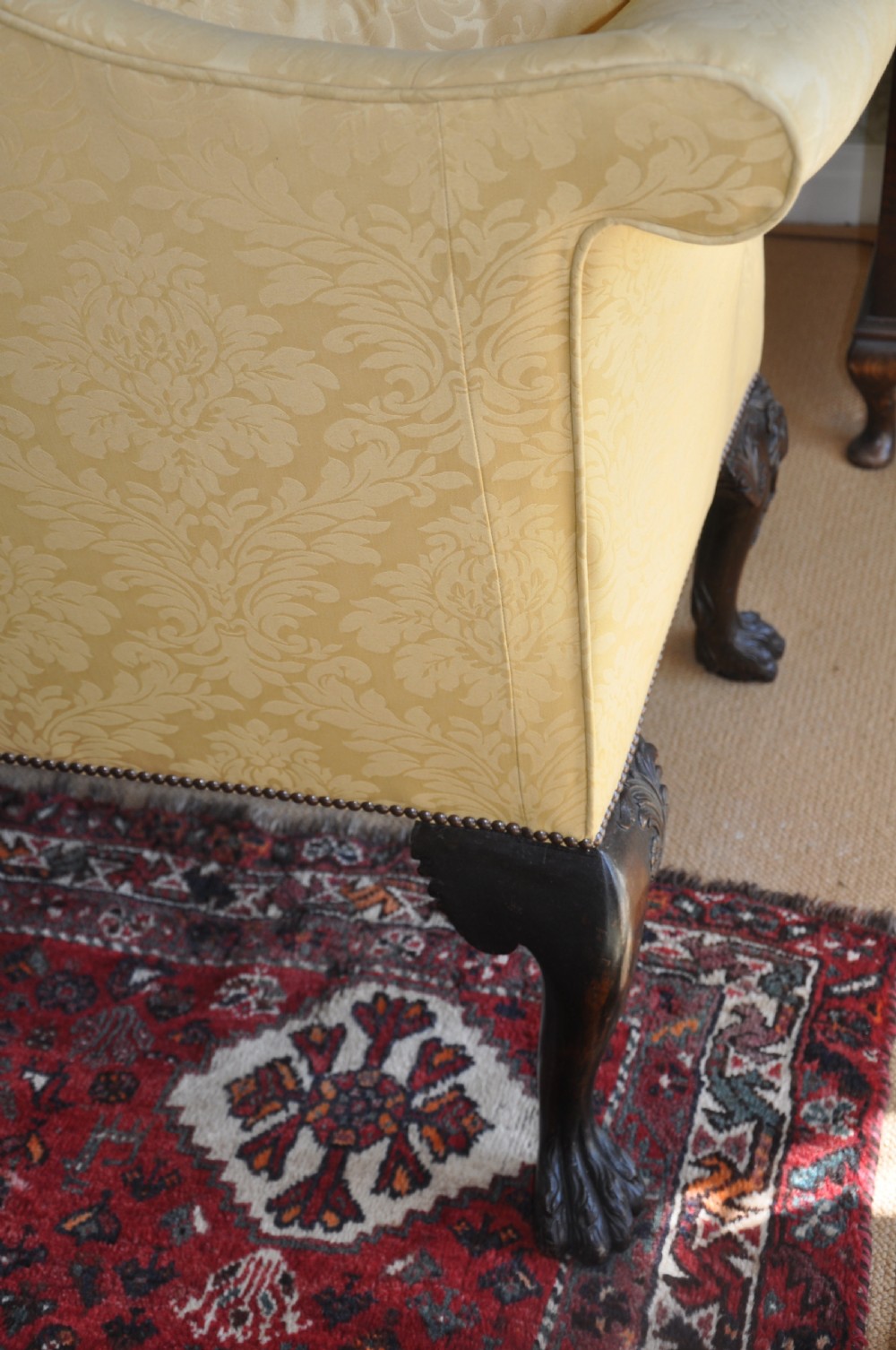 A 19th-century camelback settee upholstered in patterned yellow damask fabric with brass studding and carved mahogany legs featuring lion mask motifs. View X
