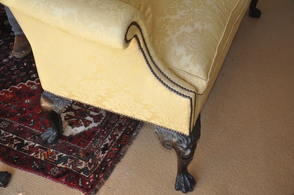A 19th-century camelback settee upholstered in patterned yellow damask fabric with brass studding and carved mahogany legs featuring lion mask motifs. View XI