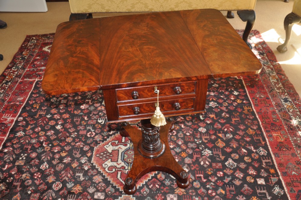 A Regency flame mahogany Pembroke table featuring two drop leaves, two small drawers with turned wooden handles, a carved turned pedestal support, and a quadruped platform base.