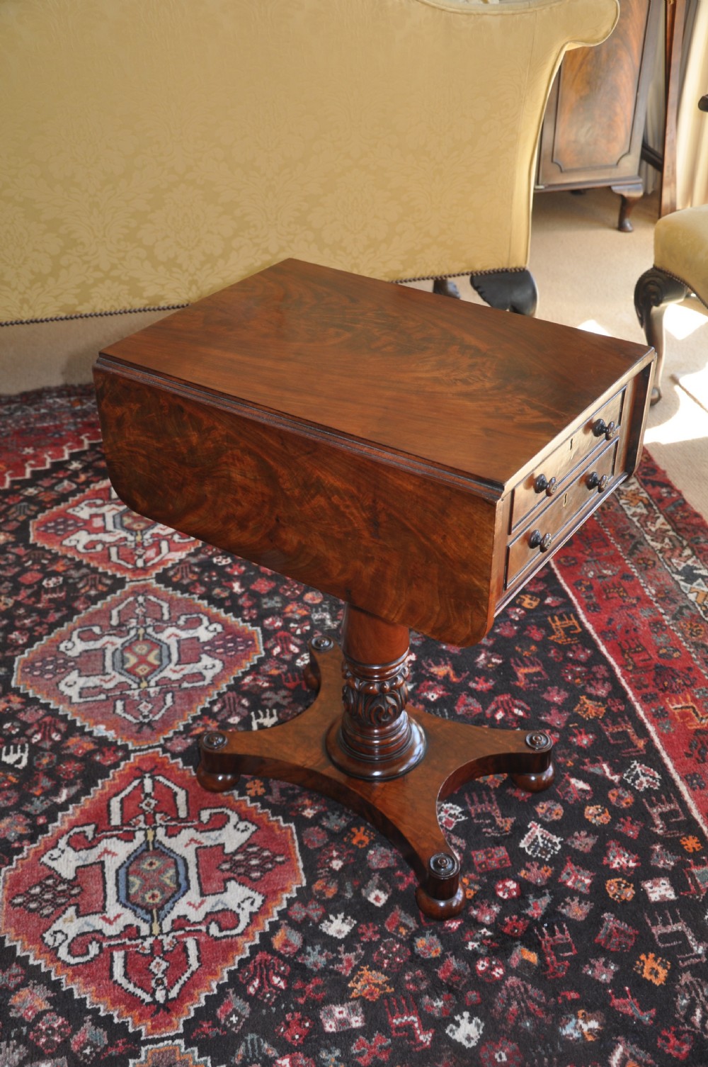 A Regency flame mahogany Pembroke table featuring two drop leaves, two small drawers with turned wooden handles, a carved turned pedestal support, and a quadruped platform base. View III