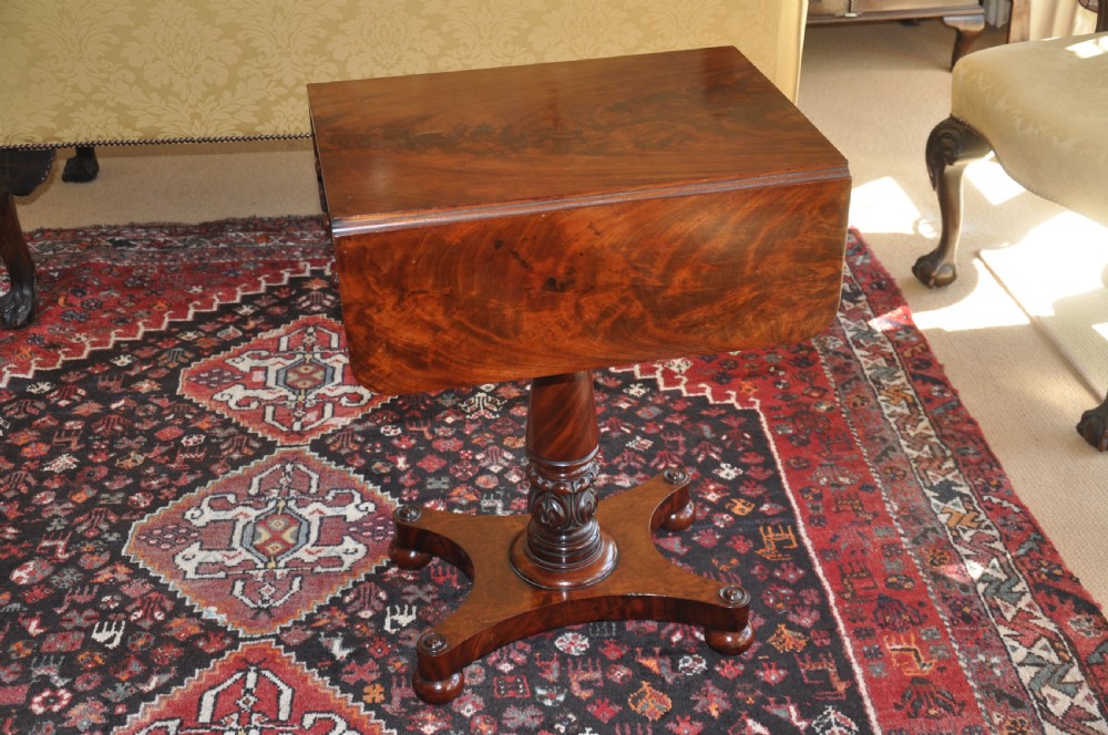 A Regency flame mahogany Pembroke table featuring two drop leaves, two small drawers with turned wooden handles, a carved turned pedestal support, and a quadruped platform base. View IV