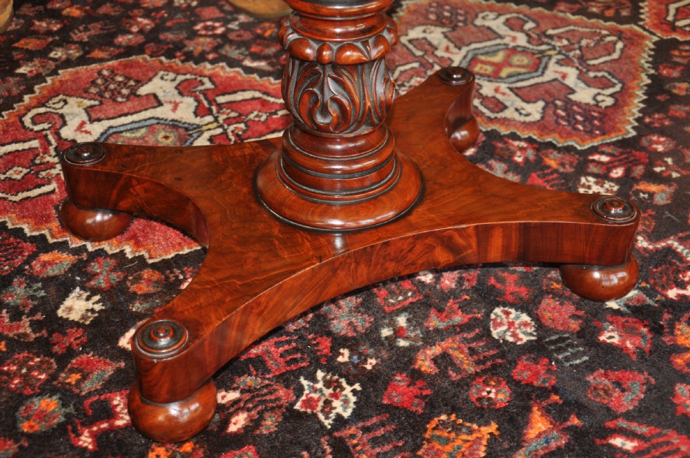 A Regency flame mahogany Pembroke table featuring two drop leaves, two small drawers with turned wooden handles, a carved turned pedestal support, and a quadruped platform base. View V