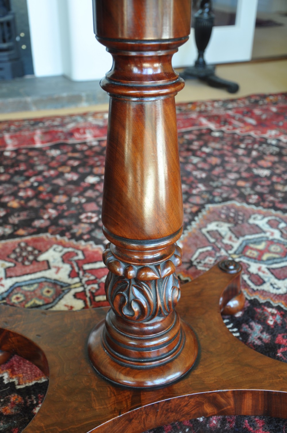 A Regency flame mahogany Pembroke table featuring two drop leaves, two small drawers with turned wooden handles, a carved turned pedestal support, and a quadruped platform base. View VI