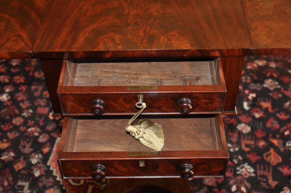 A Regency flame mahogany Pembroke table featuring two drop leaves, two small drawers with turned wooden handles, a carved turned pedestal support, and a quadruped platform base. View VII
