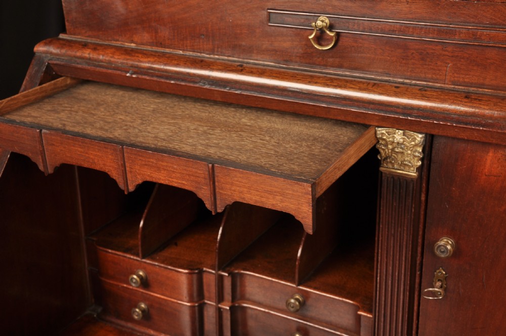 An 18th-century mahogany bureau cabinet featuring an architectural pediment top, two panelled upper doors, a slant-front writing desk, and lower drawers on bracket feet. View X