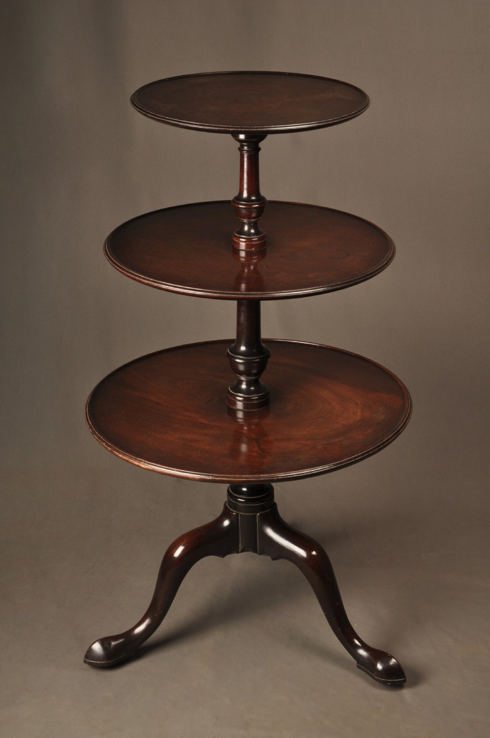 An 18th-century mahogany three-tiered dumb waiter featuring graduated dished trays, a turned central column, and tripod cabriole legs.