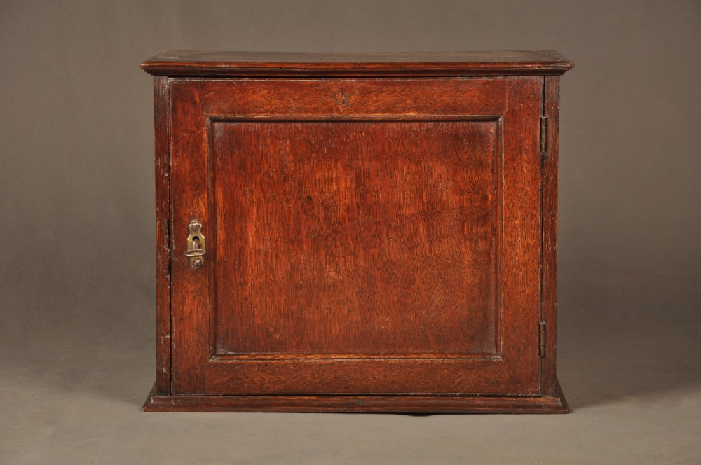 A mid-18th-century oak spice cupboard featuring a single fielded panel door with a brass keyhole escutcheon and a moulded base.