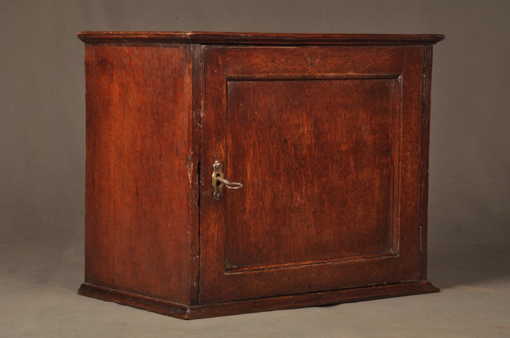 A mid-18th-century oak spice cupboard featuring a single fielded panel door with a brass keyhole escutcheon and a moulded base. View II