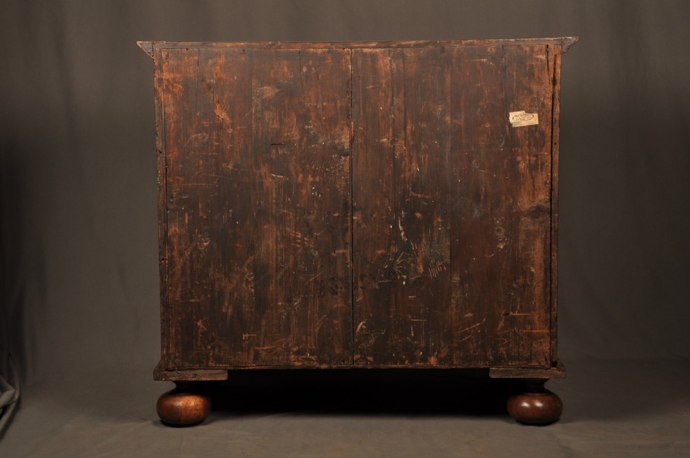 A seventeenth-century olive oyster veneered chest of drawers featuring two short drawers above three long drawers, brass drop handles, and turned bun feet. View XI