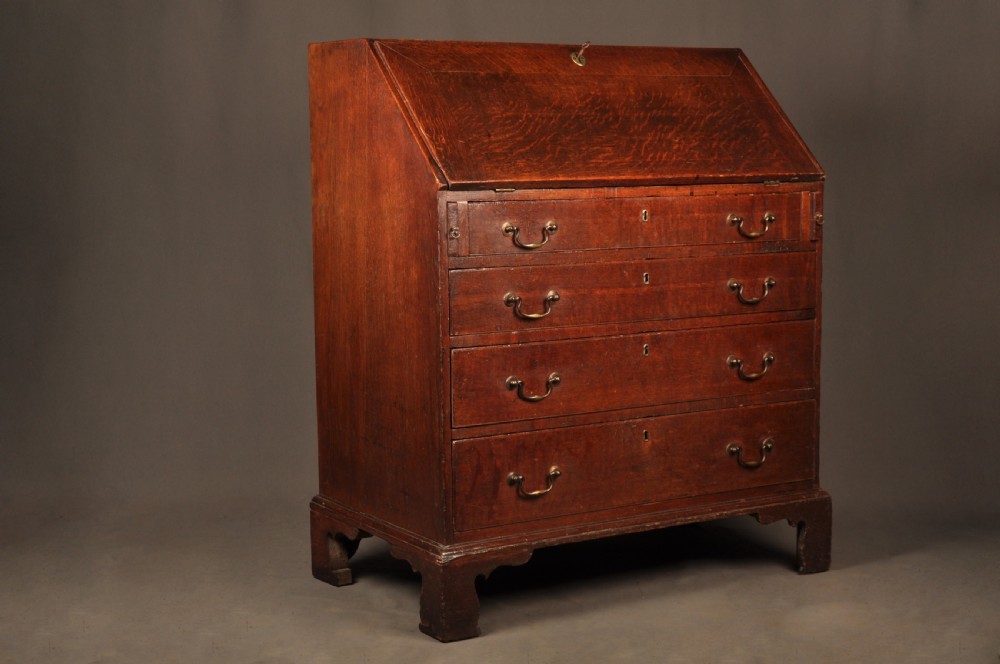 A mid-18th-century warm brown oak slant-front writing bureau featuring four graduated drawers with brass swan-neck handles and bracket feet. View II