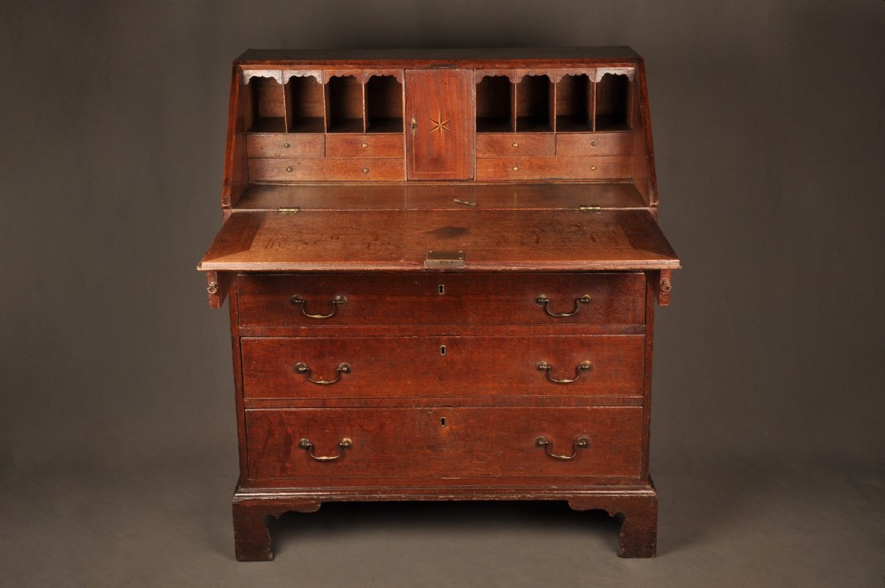 A mid-18th-century warm brown oak slant-front writing bureau featuring four graduated drawers with brass swan-neck handles and bracket feet. View IV
