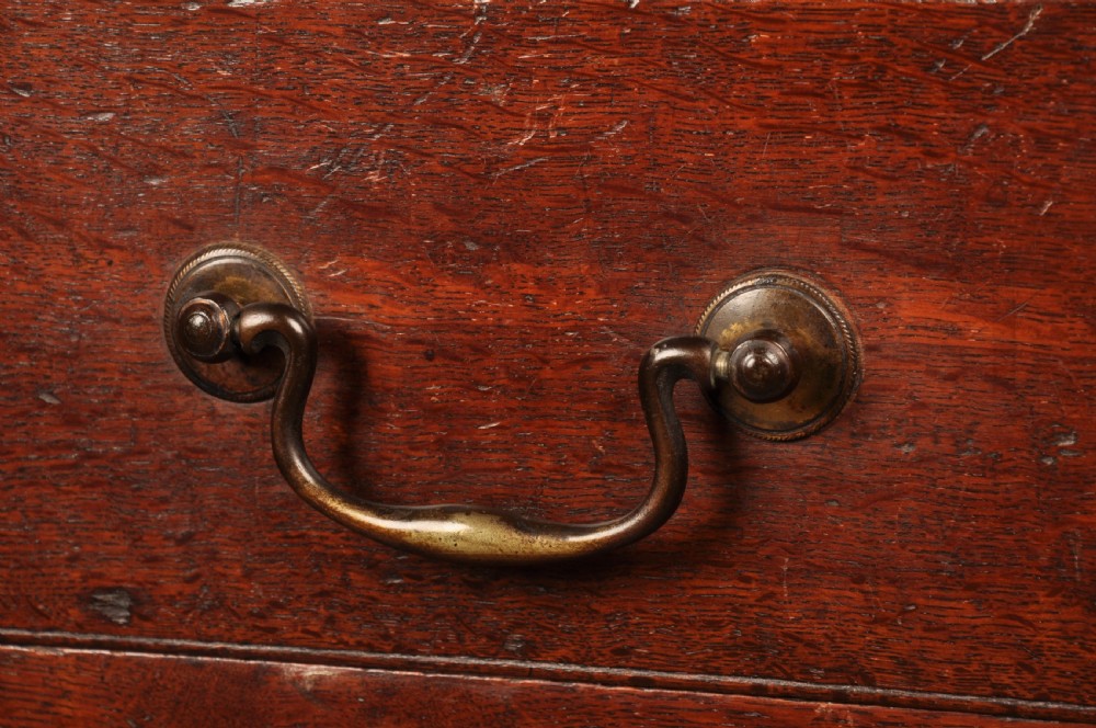A mid-18th-century warm brown oak slant-front writing bureau featuring four graduated drawers with brass swan-neck handles and bracket feet. View V