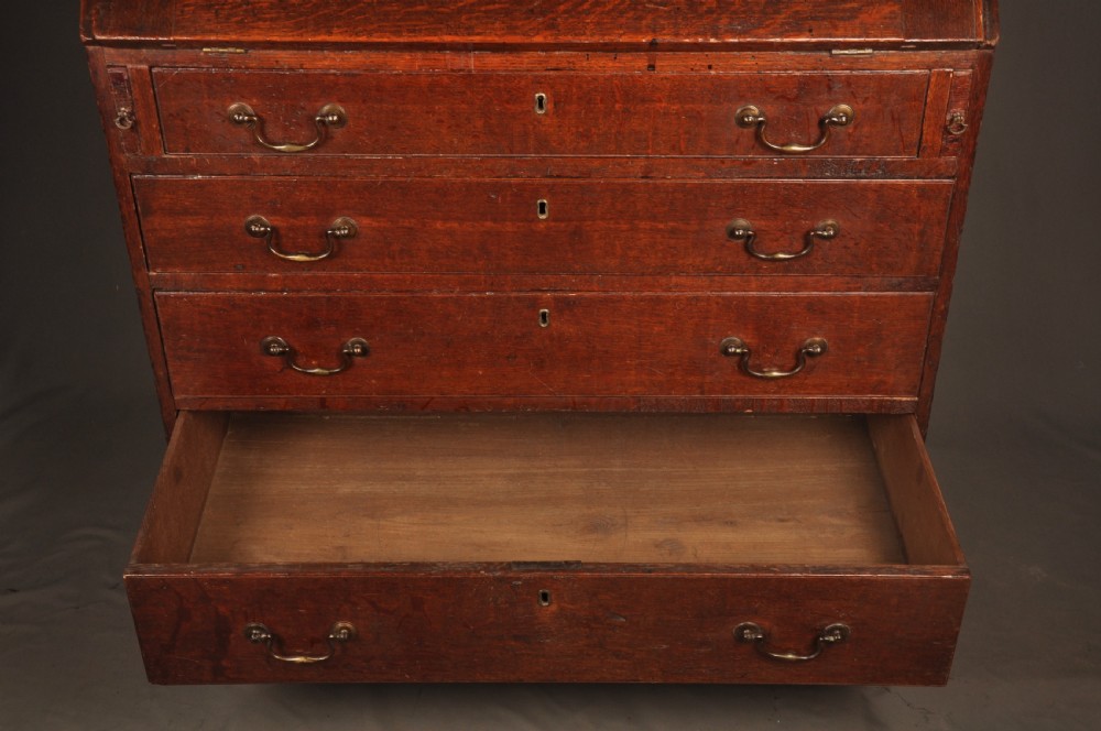 A mid-18th-century warm brown oak slant-front writing bureau featuring four graduated drawers with brass swan-neck handles and bracket feet. View IX