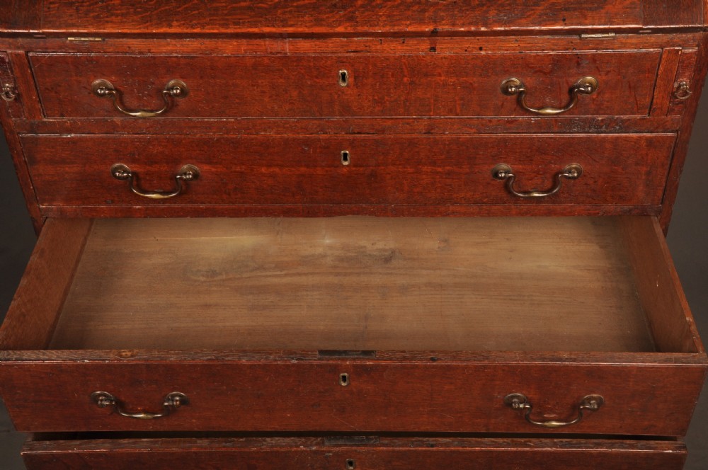 A mid-18th-century warm brown oak slant-front writing bureau featuring four graduated drawers with brass swan-neck handles and bracket feet. View X