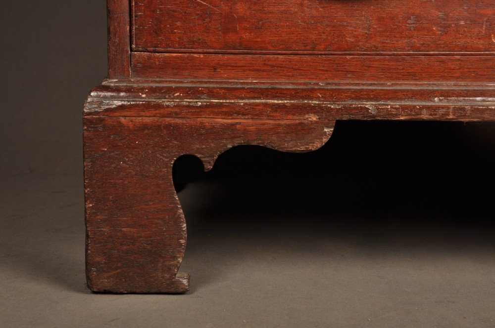 A mid-18th-century warm brown oak slant-front writing bureau featuring four graduated drawers with brass swan-neck handles and bracket feet. View XI