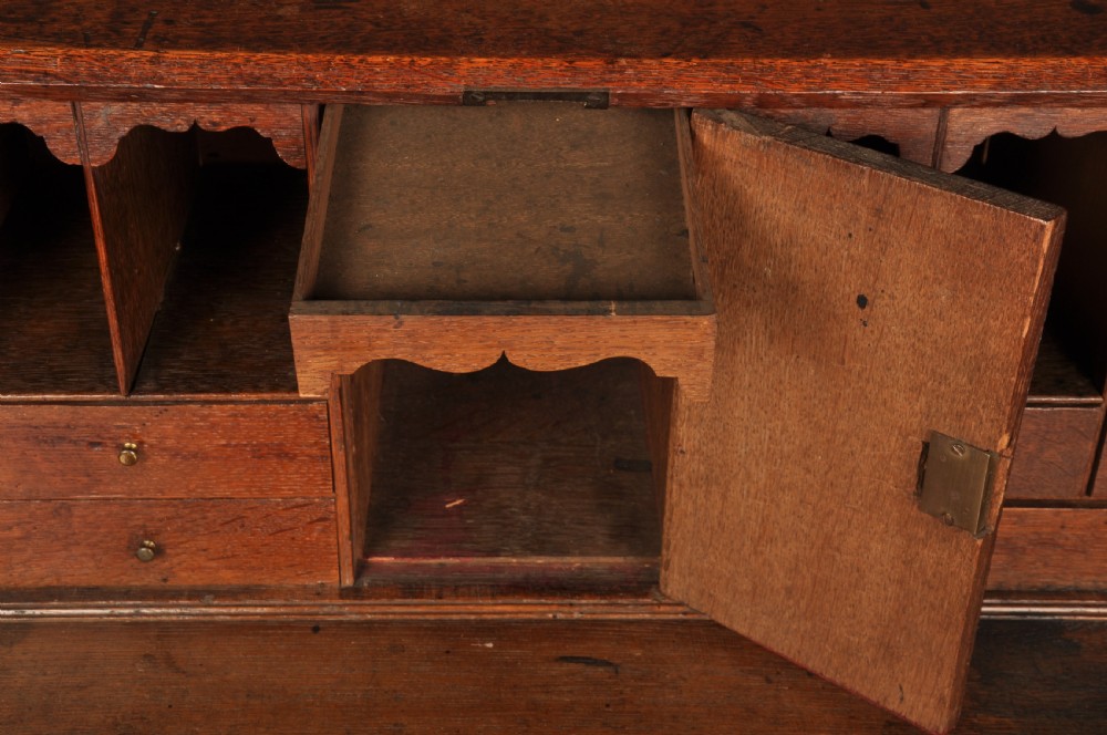 A mid-18th-century warm brown oak slant-front writing bureau featuring four graduated drawers with brass swan-neck handles and bracket feet. View XIV