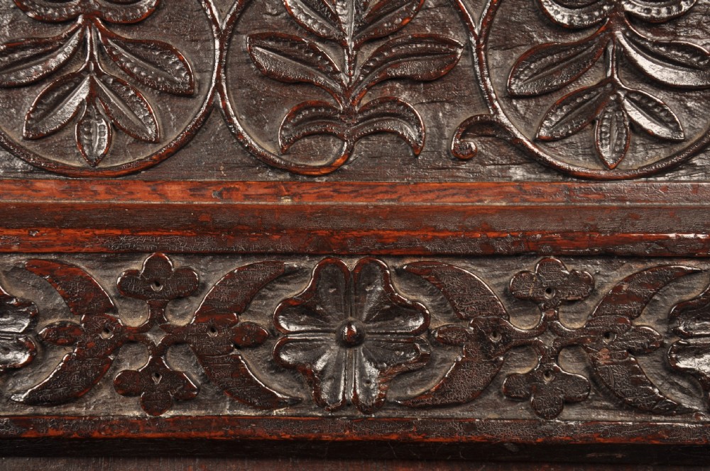 A dark oak 17th-century box settle featuring a high panelled back with carved floral friezes, turned finials, shaped armrests, and a lifted seat exposing a storage base. View IV