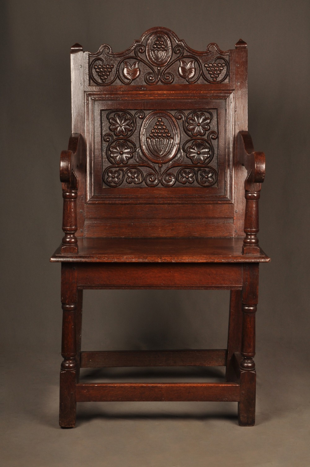 A seventeenth-century dark oak wainscot armchair featuring a carved back panel with floral motifs, turned supports, and shaped armrests. View IV