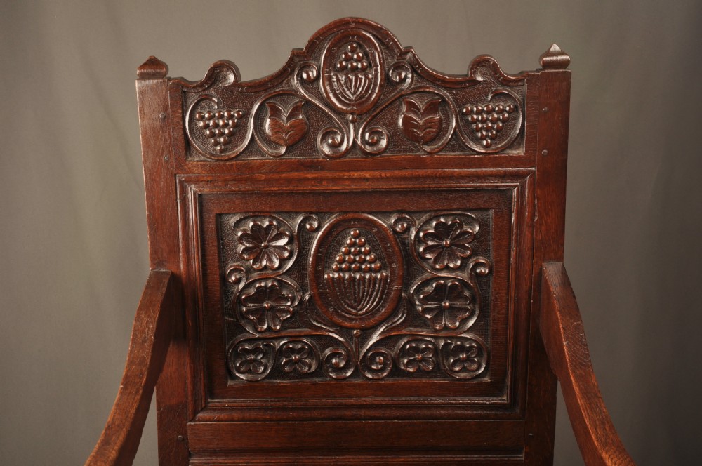 A seventeenth-century dark oak wainscot armchair featuring a carved back panel with floral motifs, turned supports, and shaped armrests. View VI