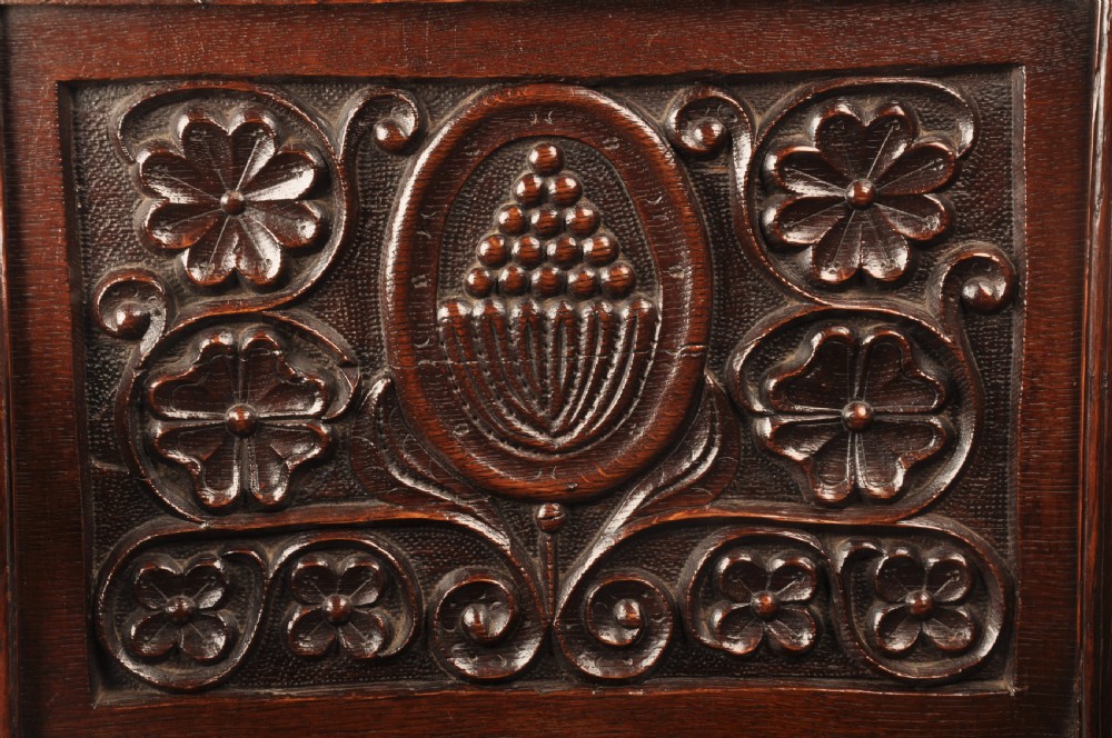 A seventeenth-century dark oak wainscot armchair featuring a carved back panel with floral motifs, turned supports, and shaped armrests. View VII