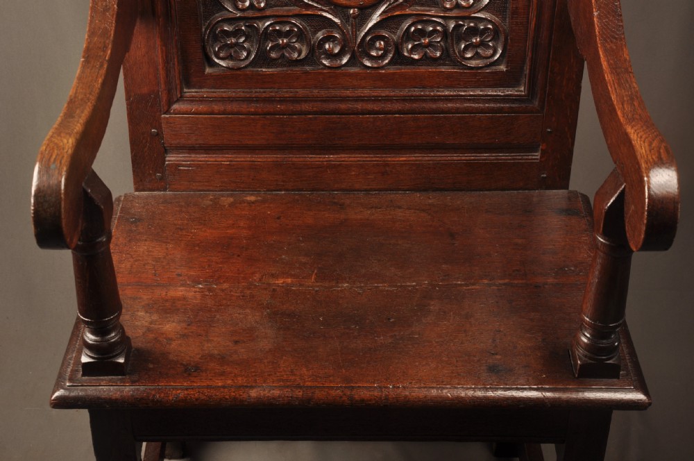 A seventeenth-century dark oak wainscot armchair featuring a carved back panel with floral motifs, turned supports, and shaped armrests. View VIII