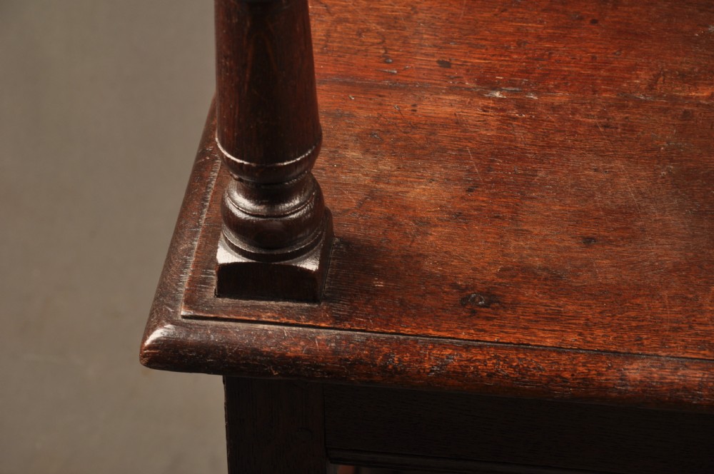 A seventeenth-century dark oak wainscot armchair featuring a carved back panel with floral motifs, turned supports, and shaped armrests. View IX