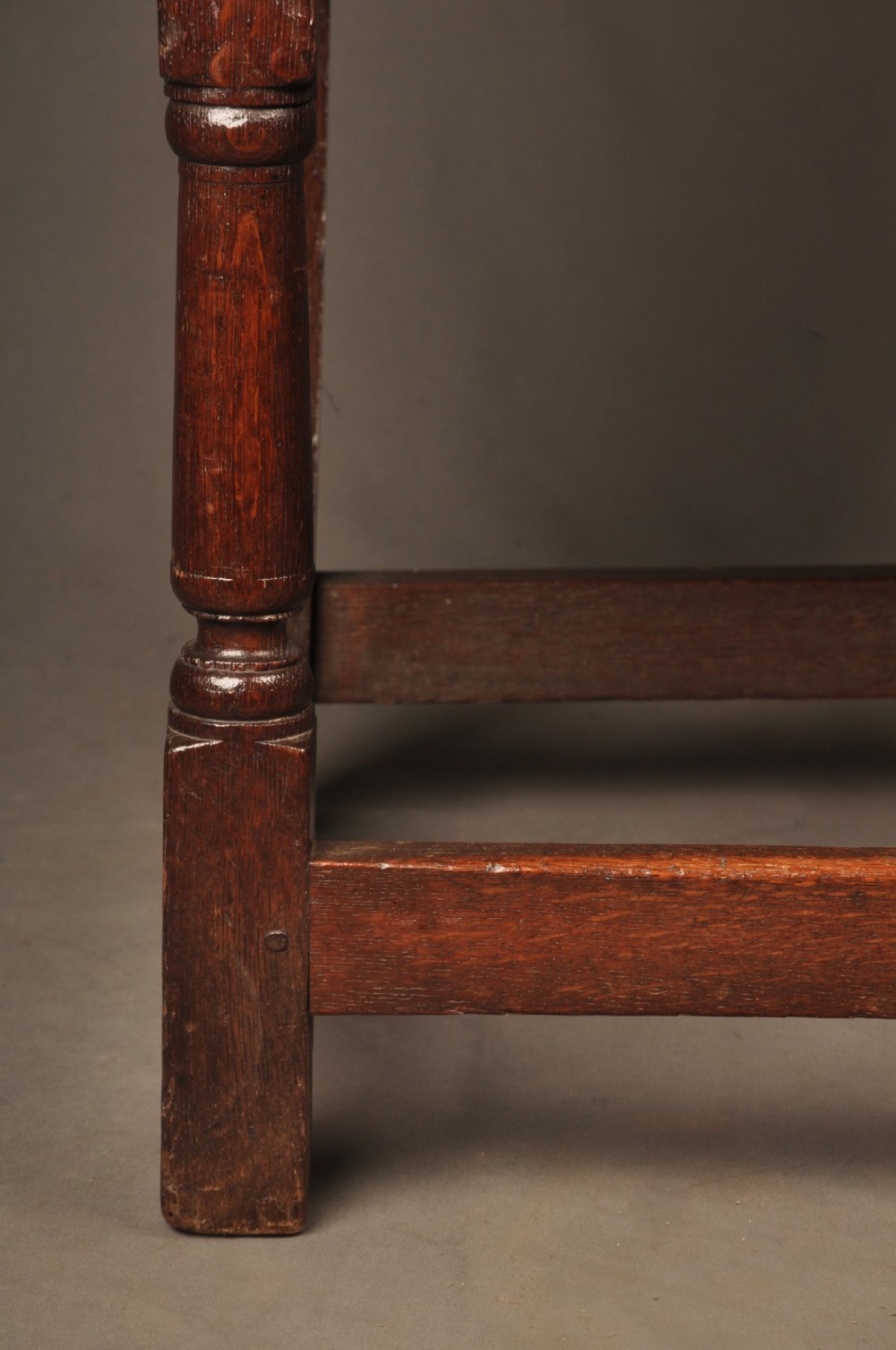 A seventeenth-century dark oak wainscot armchair featuring a carved back panel with floral motifs, turned supports, and shaped armrests. View XII