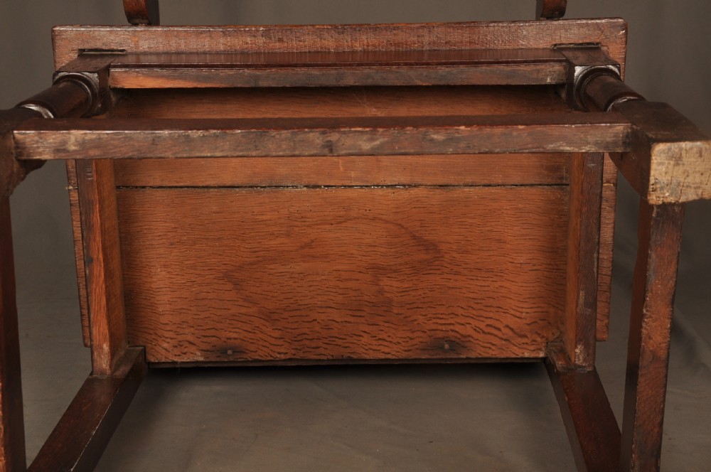 A seventeenth-century dark oak wainscot armchair featuring a carved back panel with floral motifs, turned supports, and shaped armrests. View XIV