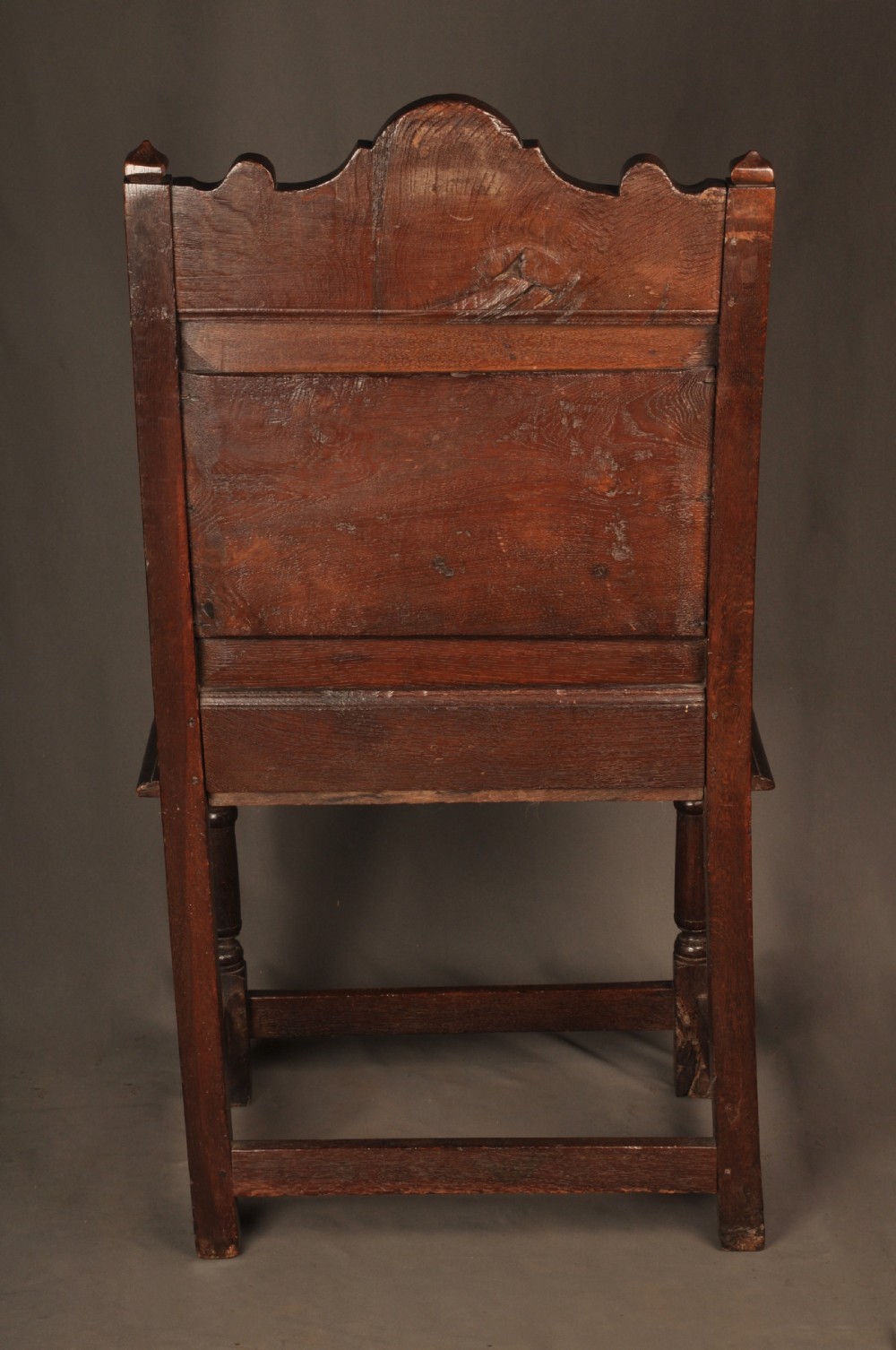 A seventeenth-century dark oak wainscot armchair featuring a carved back panel with floral motifs, turned supports, and shaped armrests. View XV