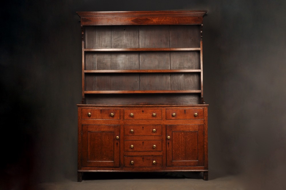 An eighteenth-century warm brown oak dresser featuring an upper three-tier open plate rack above a lower cabinet with drawers and panelled cupboard doors.
