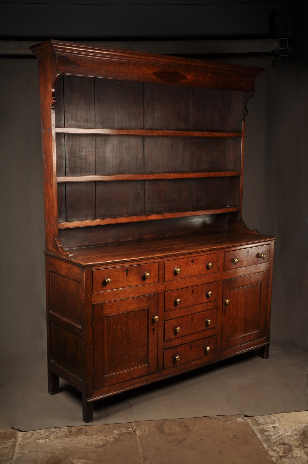 An eighteenth-century warm brown oak dresser featuring an upper three-tier open plate rack above a lower cabinet with drawers and panelled cupboard doors. View II
