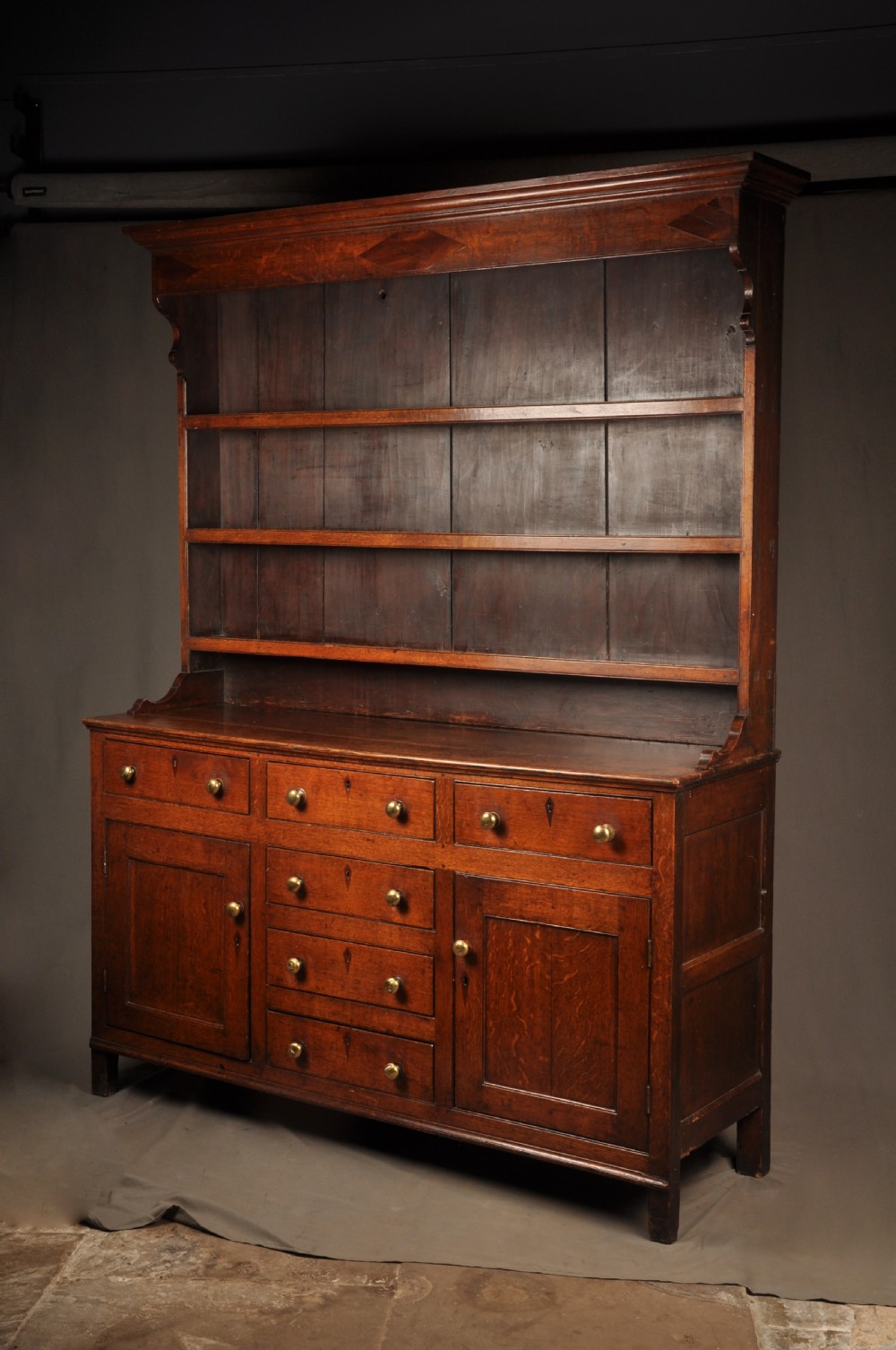 An eighteenth-century warm brown oak dresser featuring an upper three-tier open plate rack above a lower cabinet with drawers and panelled cupboard doors. View III