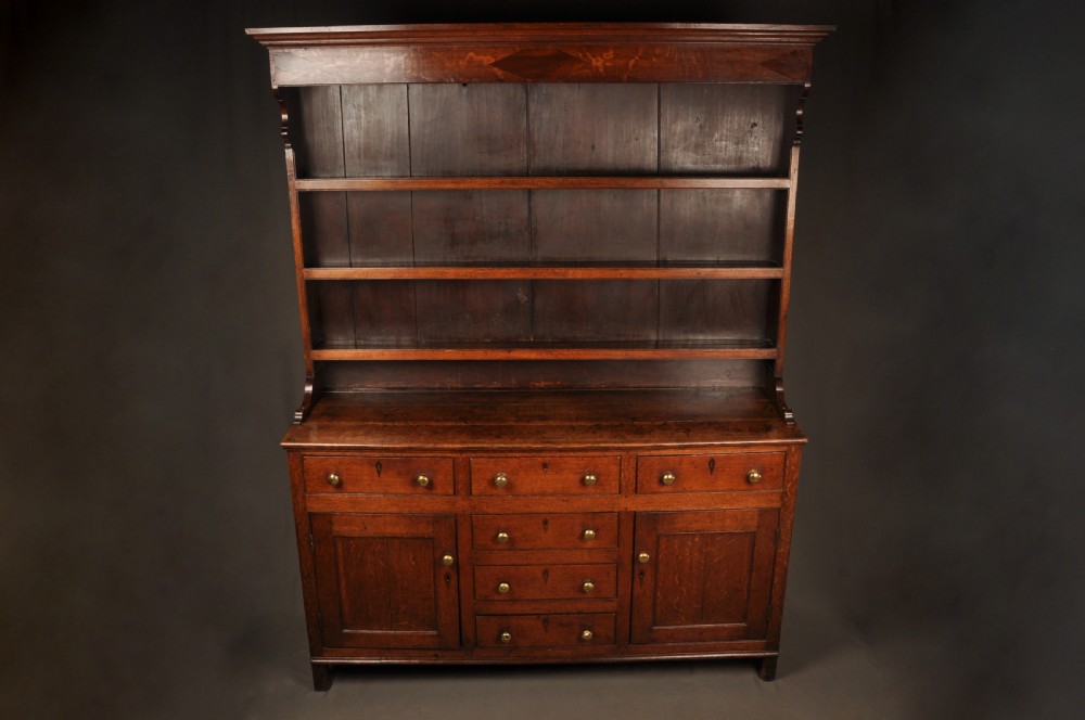 An eighteenth-century warm brown oak dresser featuring an upper three-tier open plate rack above a lower cabinet with drawers and panelled cupboard doors. View IV